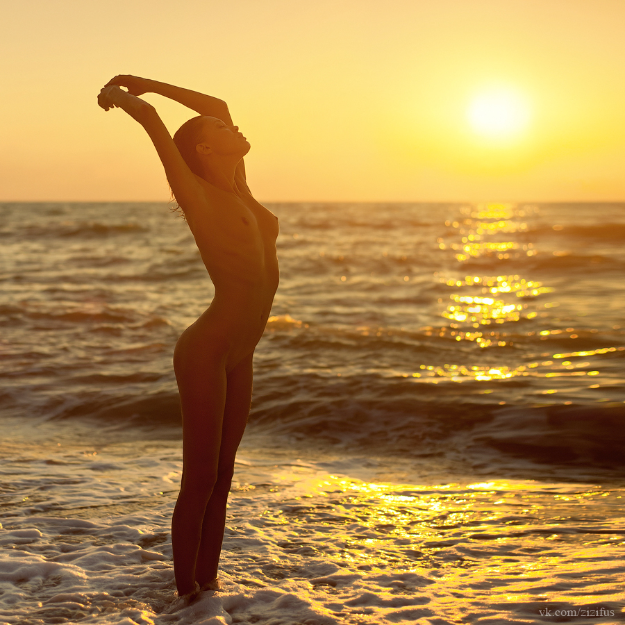 nude woman stretching in the waves during sunset.